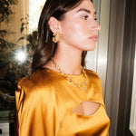 Woman wearing a mustard yellow satin dress with cut-out design, gold earrings, and necklace.